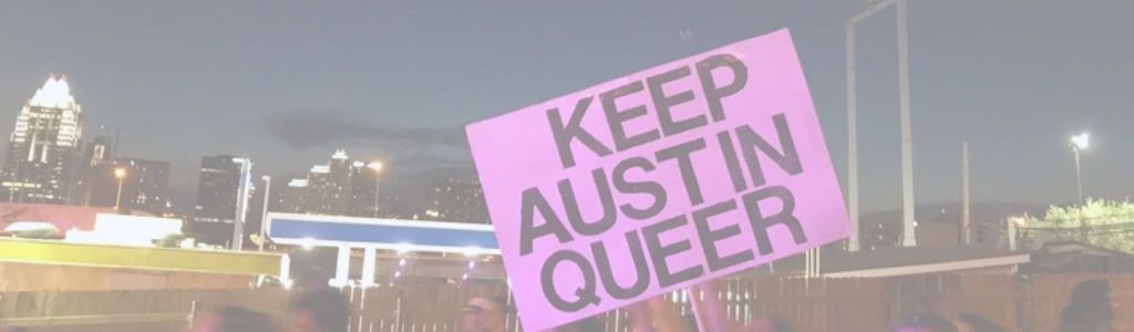 A person holding a pink sign that says “KEEP AUSTIN QUEER” in front of the Austin city skyline at night, during Queer Bomb 2018.