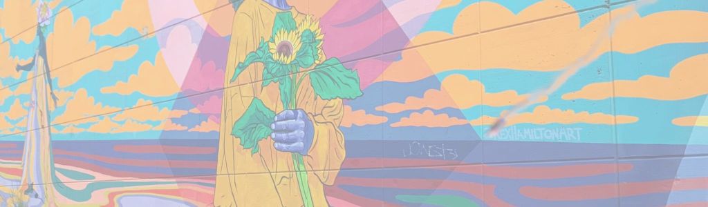 Graffiti painting on the side of an Austin, Texas bridge showing a Black woman from the neck down holding two sunflowers against a cloudy sky.