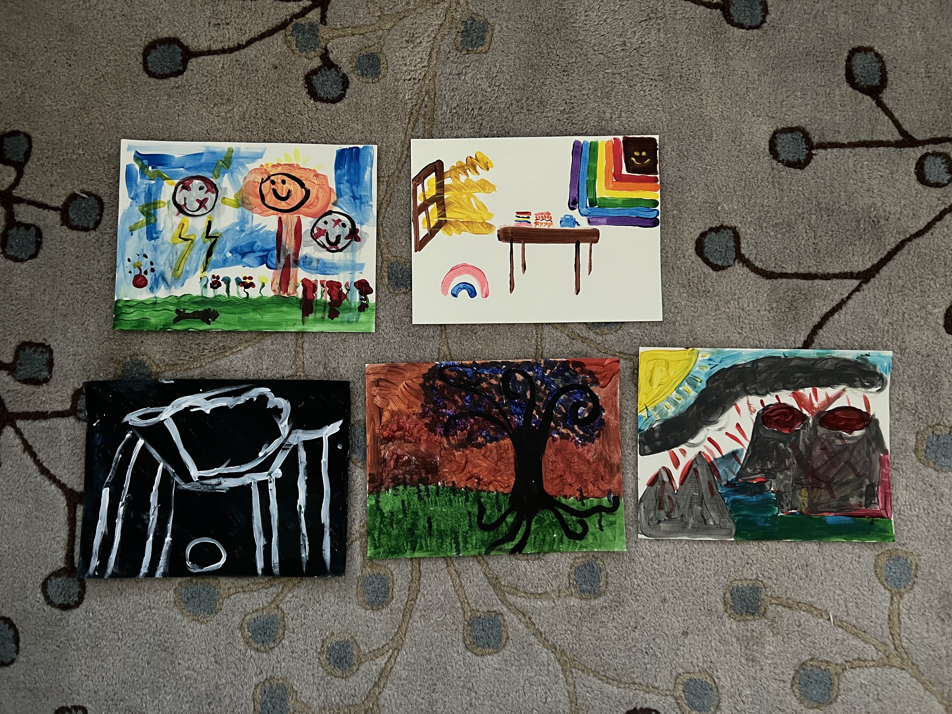 A floor display of five paintings arranged together, each exploring the theme “war and peace.” Originally painted to represent peace, the artworks were then overpainted with chaotic, darker markings symbolizing war, and finally repainted to restore peace. The final pieces show a mix of calm imagery and traces of conflict, reflecting the creative process of moving from peace to war and back to peace.